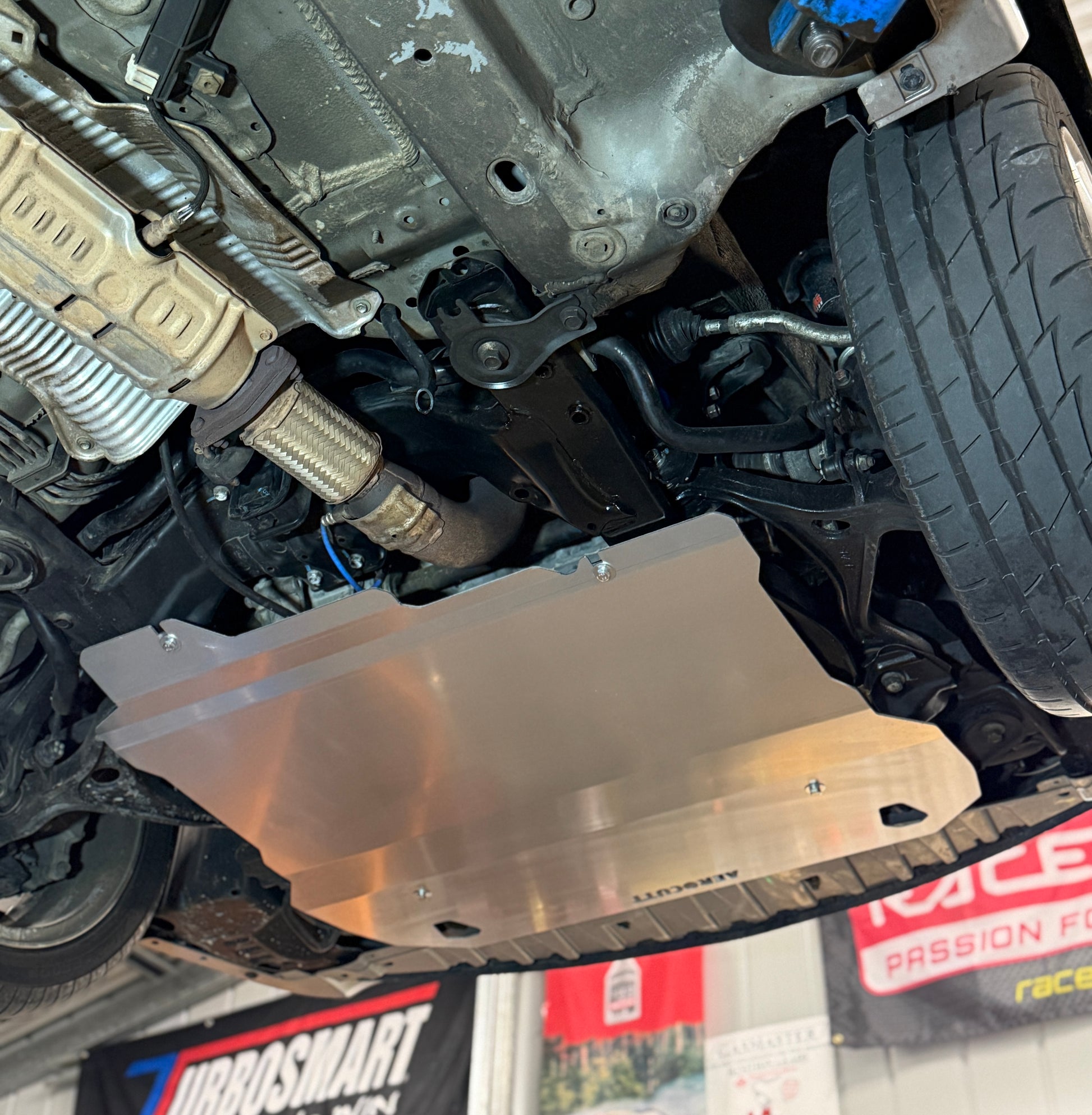 Close-up of a vehicle's undercarriage with a metal guard, visible brand logos in the background. aerocutt products 