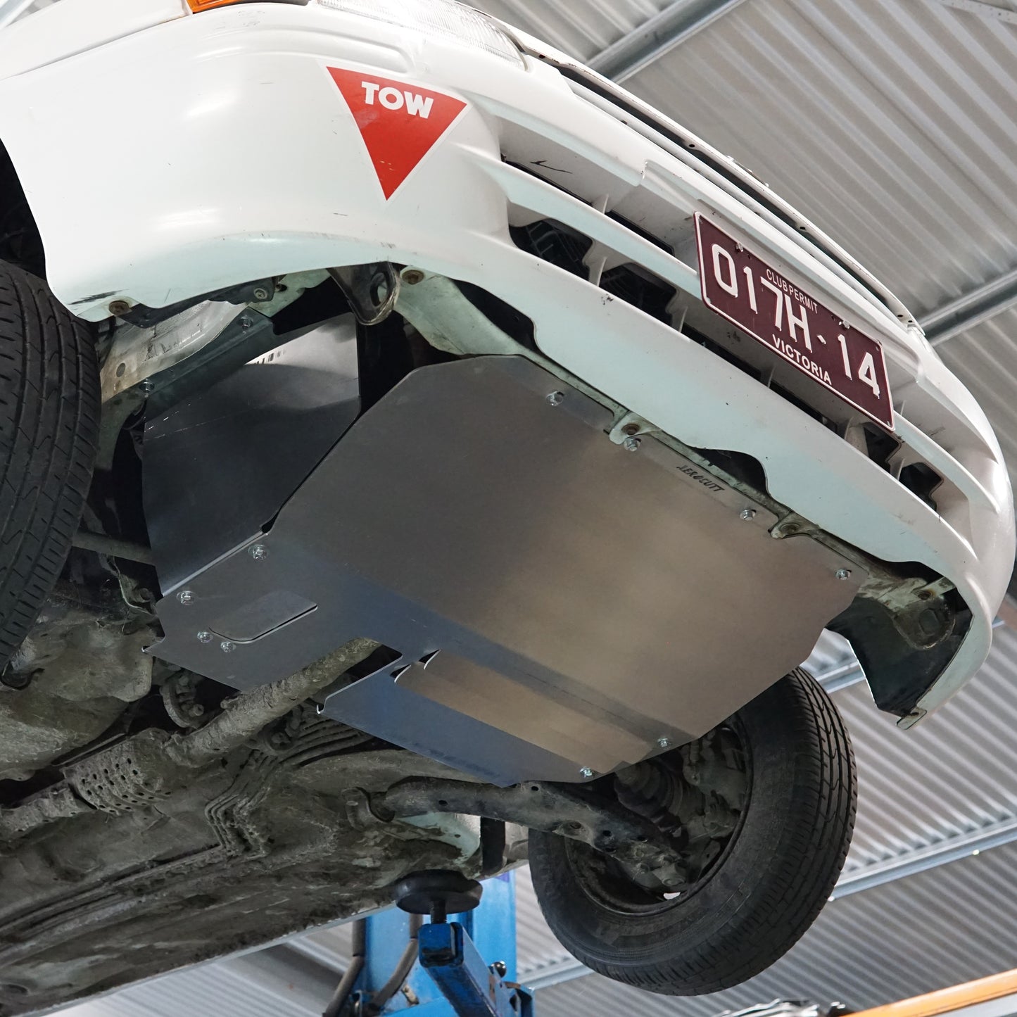 Toyota Starlet EP91 undercarriage with an Aerocutt protective metal skid plate on a lift in a garage.