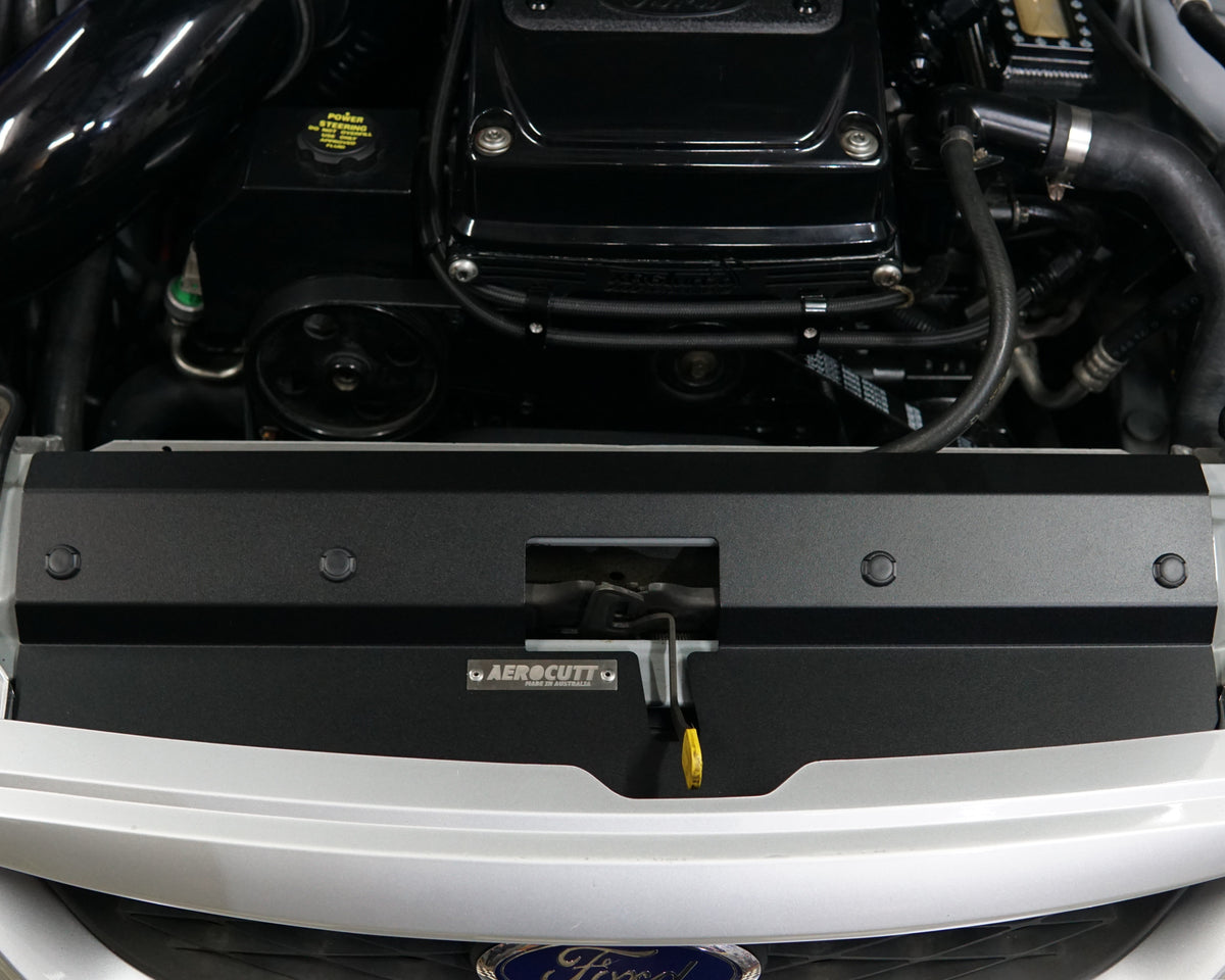A close up of a Ford Falcon BA/BF engine bay with an Aerocutt aluminium replacment air diversion plate/cooling panel in powder coated black