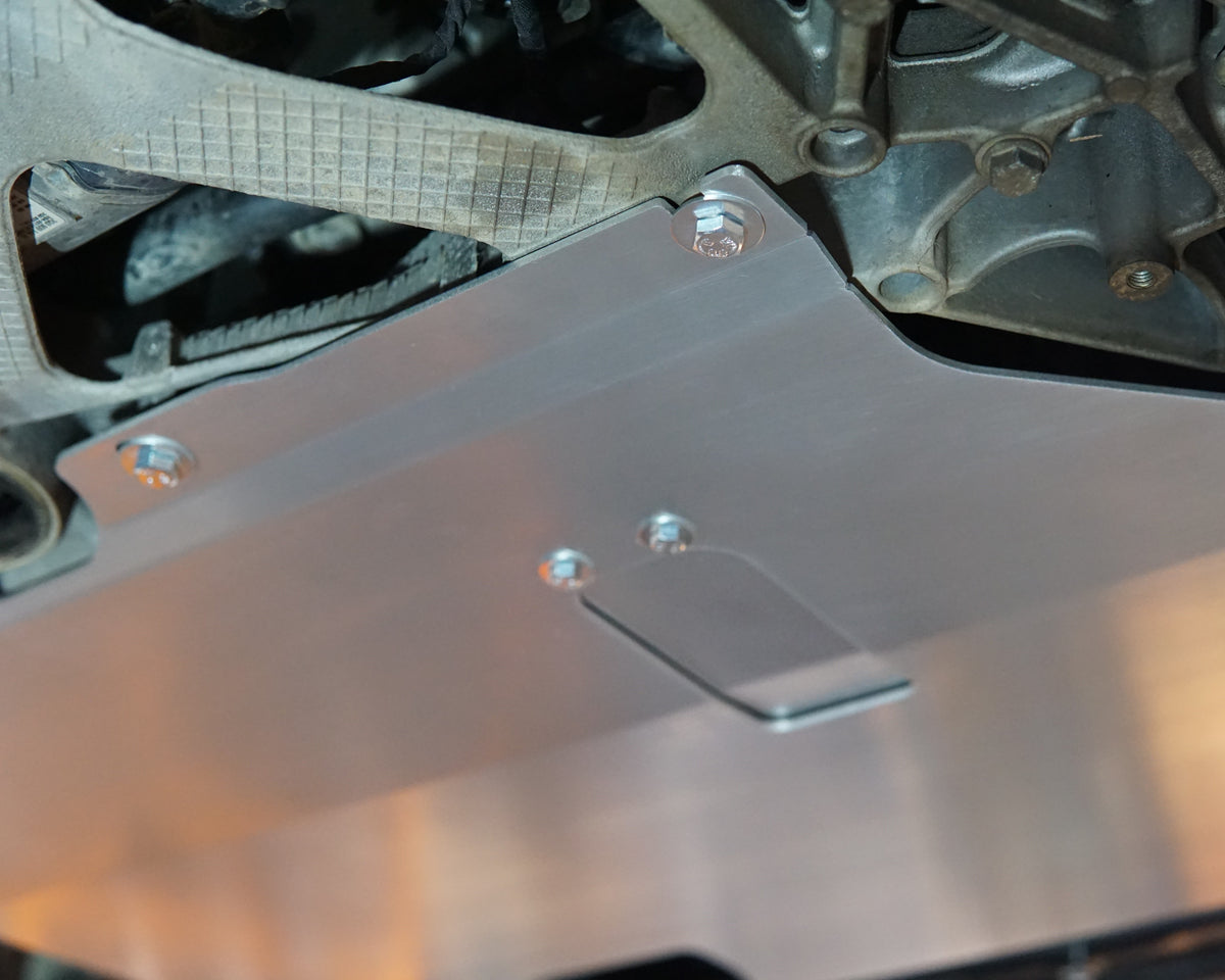 A brushed aluminum engine splash shield mounted under a Volkswagen MK7, secured with silver bolts against metal components.