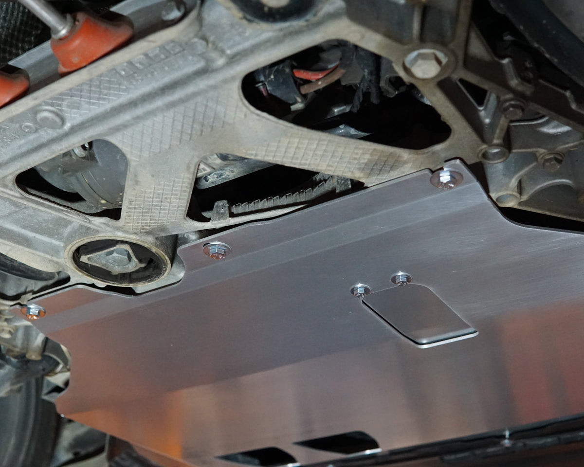 A brushed silver metal underbody shield installed on the bottom of a vehicle, secured with multiple bolts 