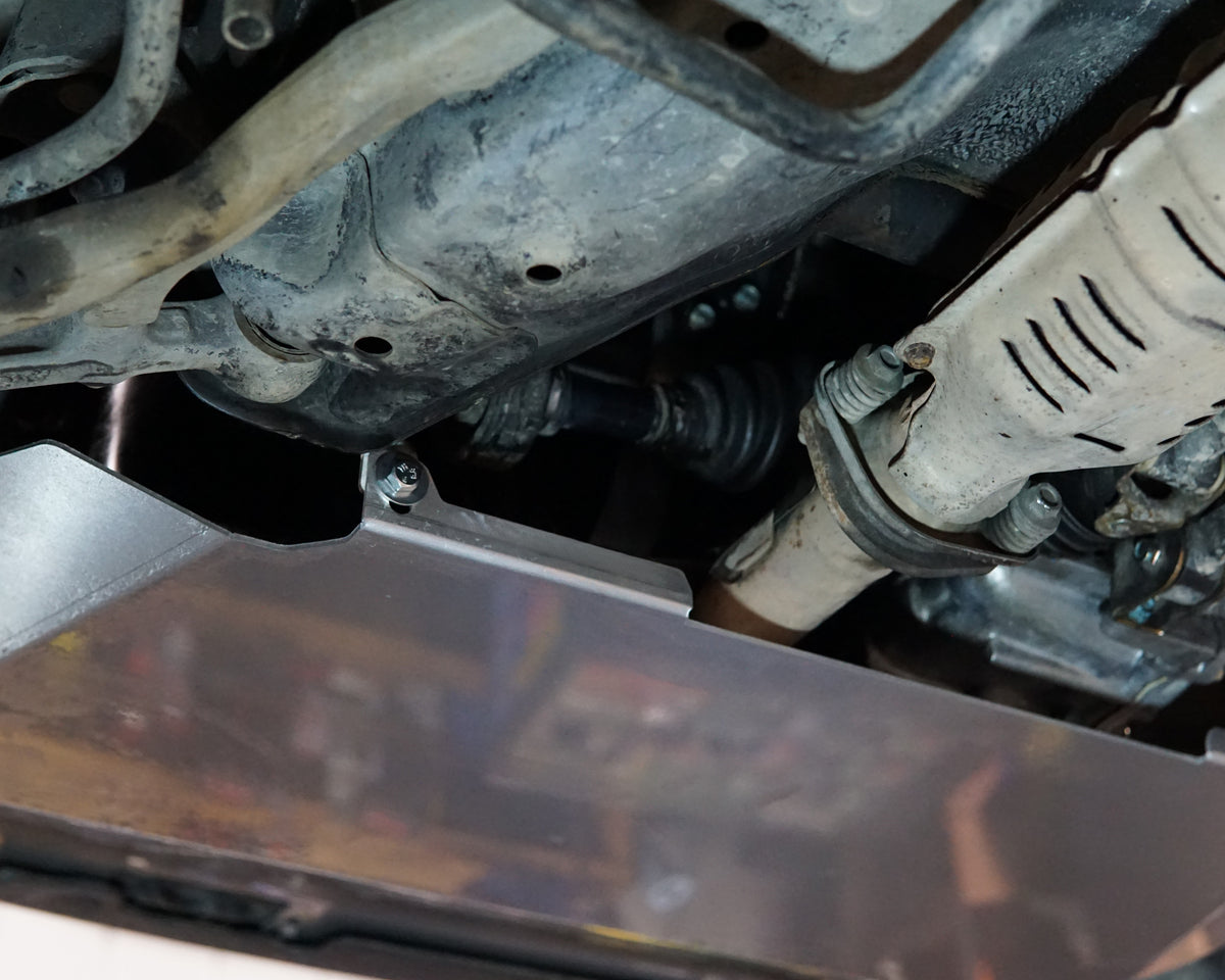 A close-up view of an EG Honda Civic undercarriage showing a dark metallic engine cover or splash panel installed beneath other mechanical parts.