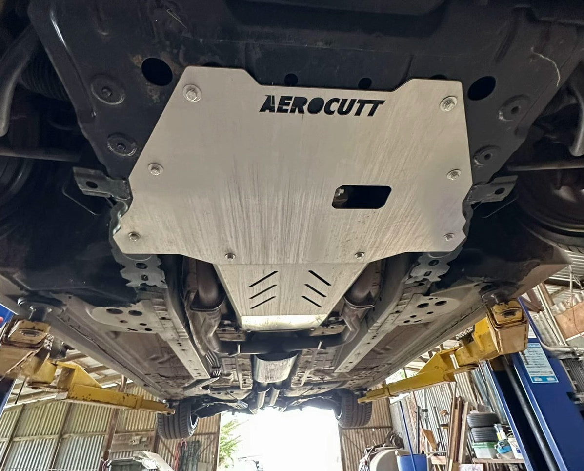 A silver Aerocutt aluminum underbody shield installed on the underside of a Holden commodore in an auto repair garage.