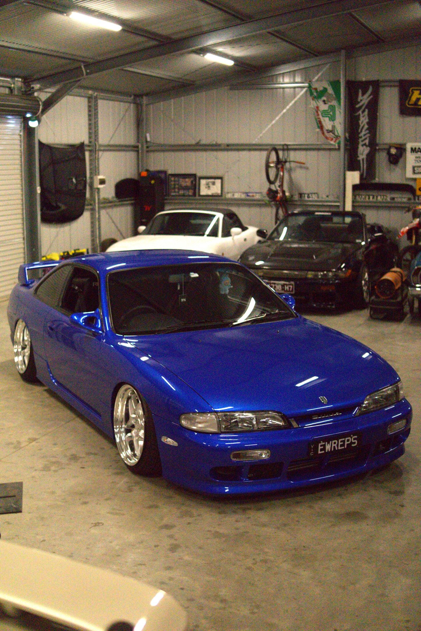 Blue car in the aerocutt garage with other vehicles and equipment in the background